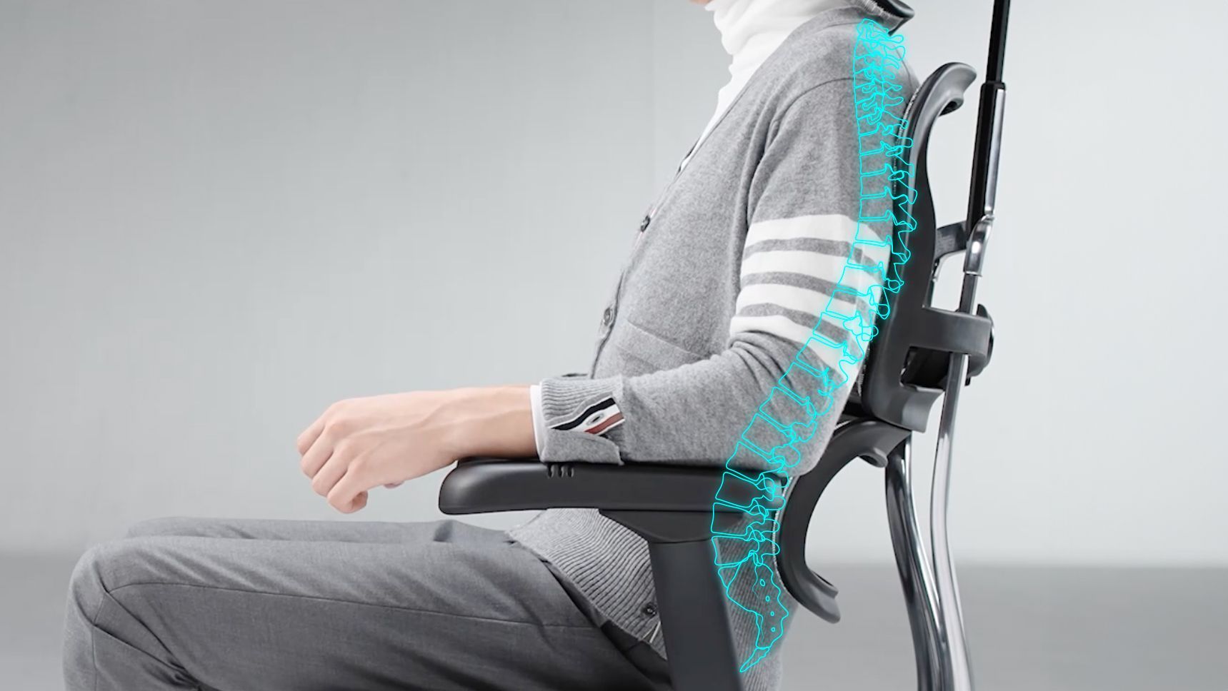The side profile of an Ergohuman office chair. A man wearing a grey shirt and trousers is sitting in the chair. He is upright and leaning back slightly. A blue illustration of a spine overlays the image to showcase how the chair supports the natural curvature of the spine.