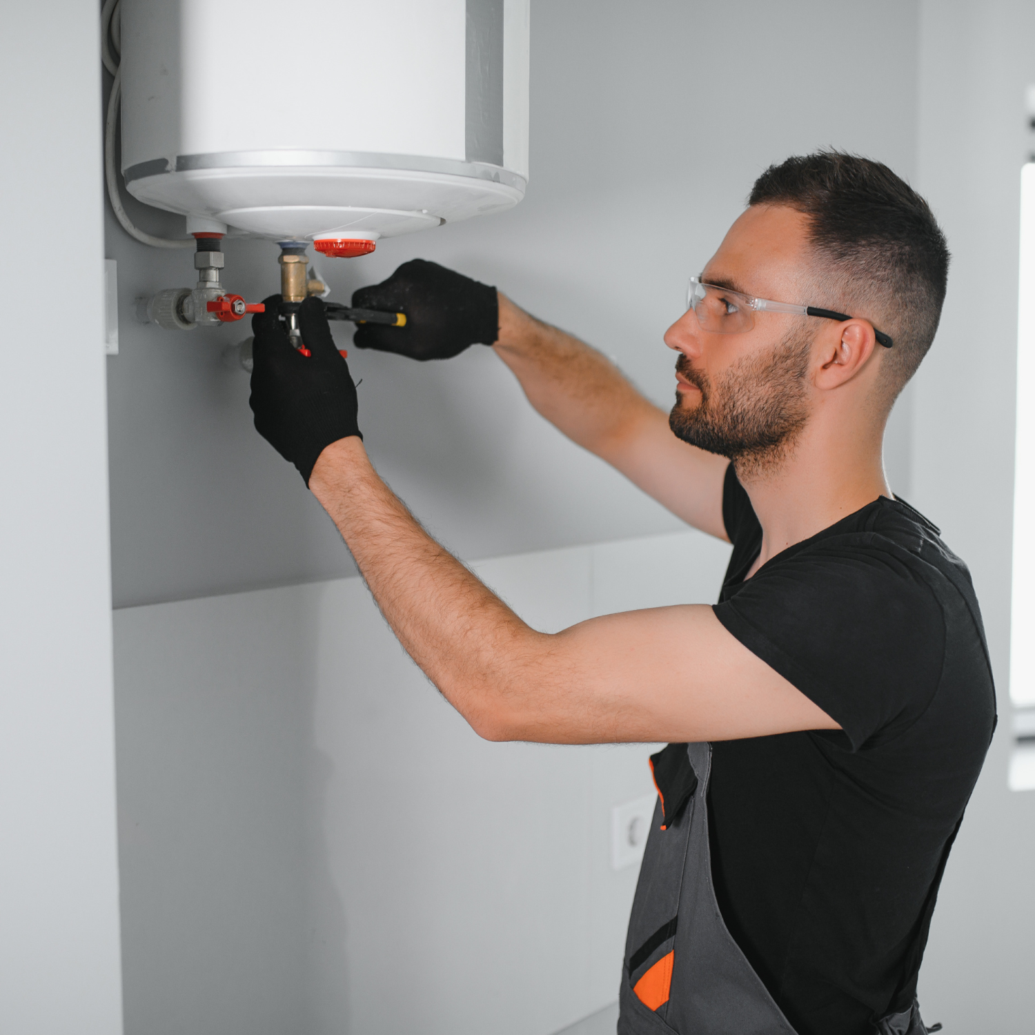 A person in safety glasses and gloves repairs a water heater.