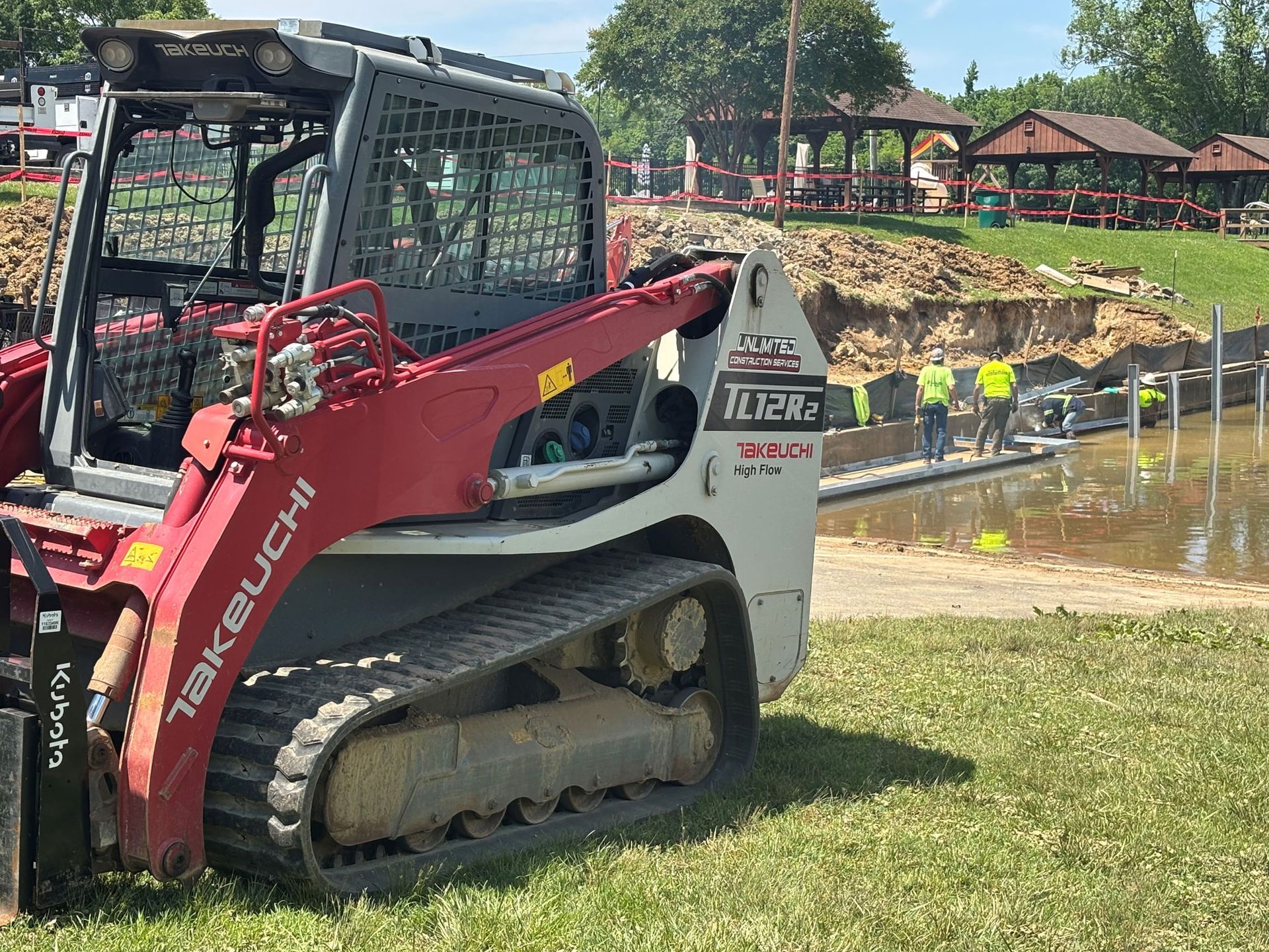 A red and white Takeuchi skid steer loader on a construction site, with workers in the background.