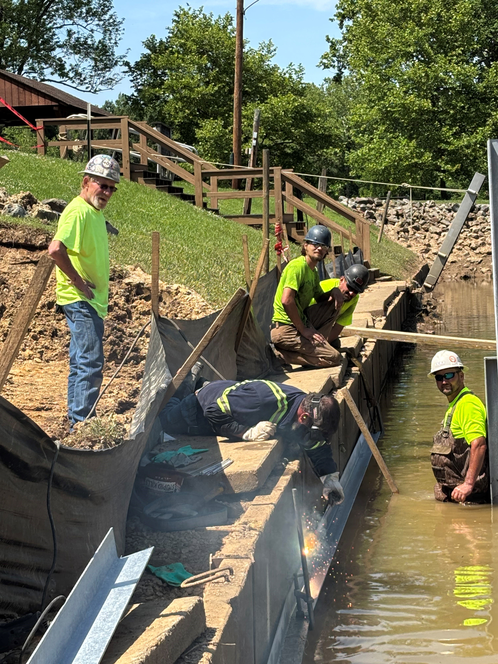 Workers connecting blue pipe to existing pipe underground.