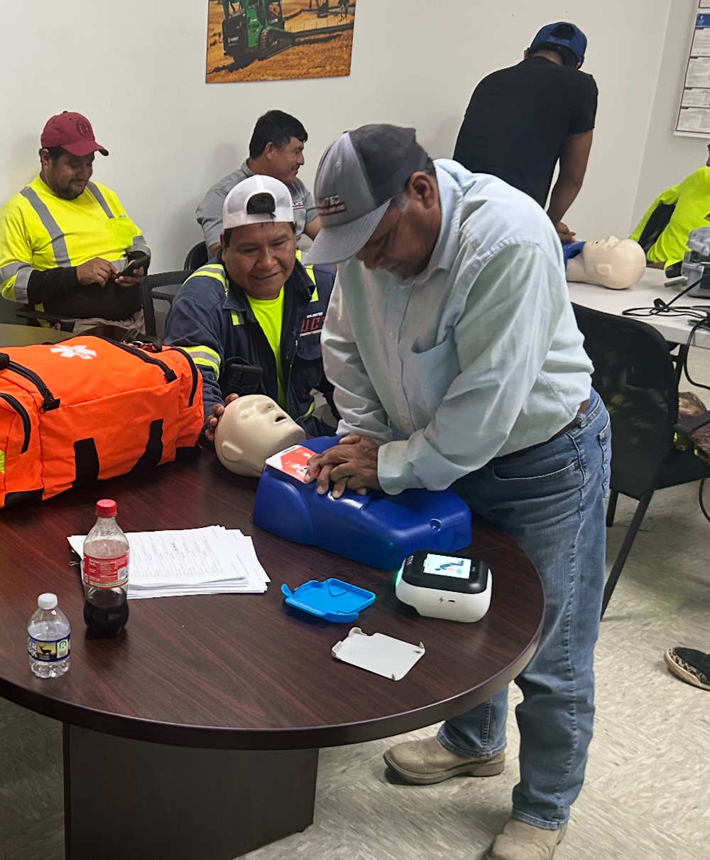 Group of workers participating in CPR training. One man demonstrates chest compressions on a mannequin.