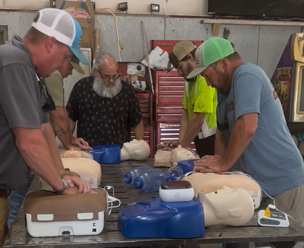 Men in a workshop practicing CPR on mannequins; some wearing hats, focused on their training.