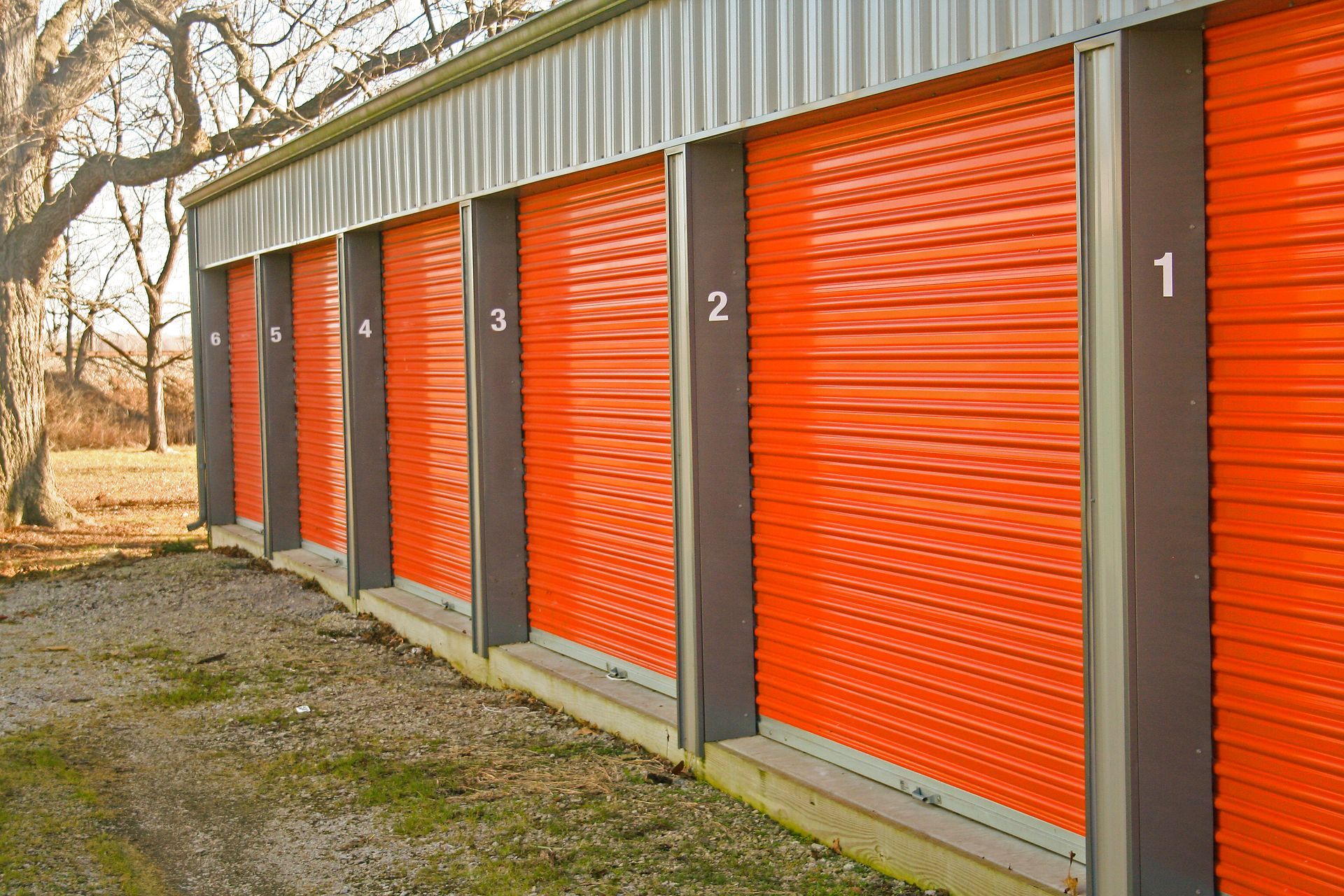 Row of orange self-storage unit doors in outdoor facility with numbered sections.