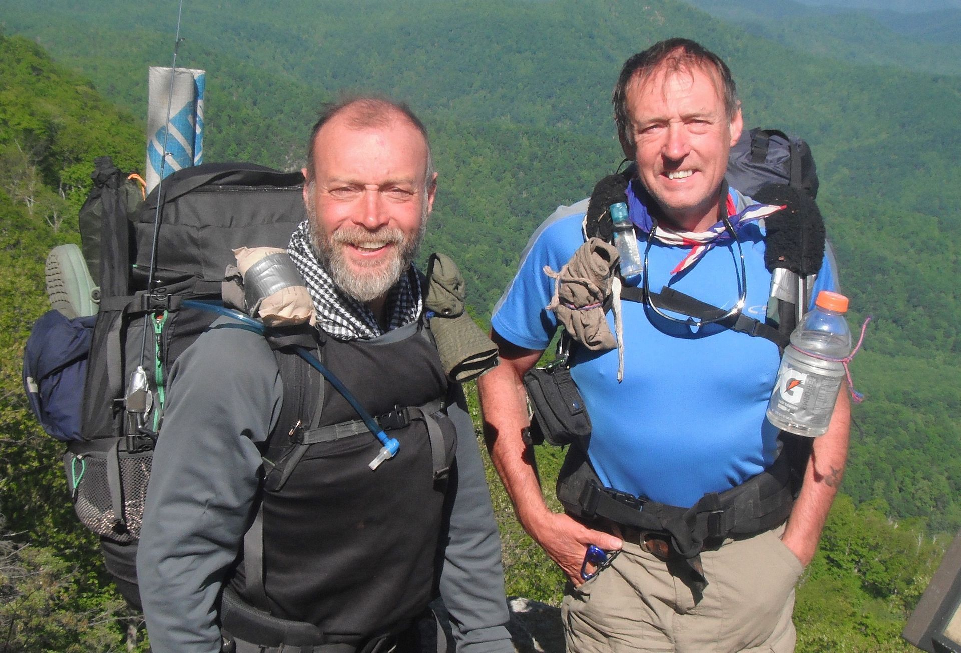 Two men standing next to each other with backpacks and a bottle of gatorade