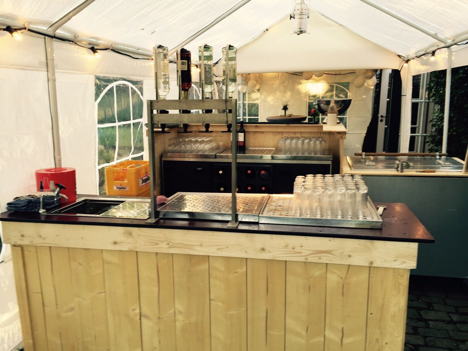 Houten bar in een witte tent, met biertaps, glazen en een spoelbak.