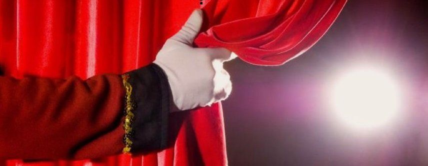 Een hand in een witte handschoen trekt het rode gordijn opzij en onthult een fel licht.