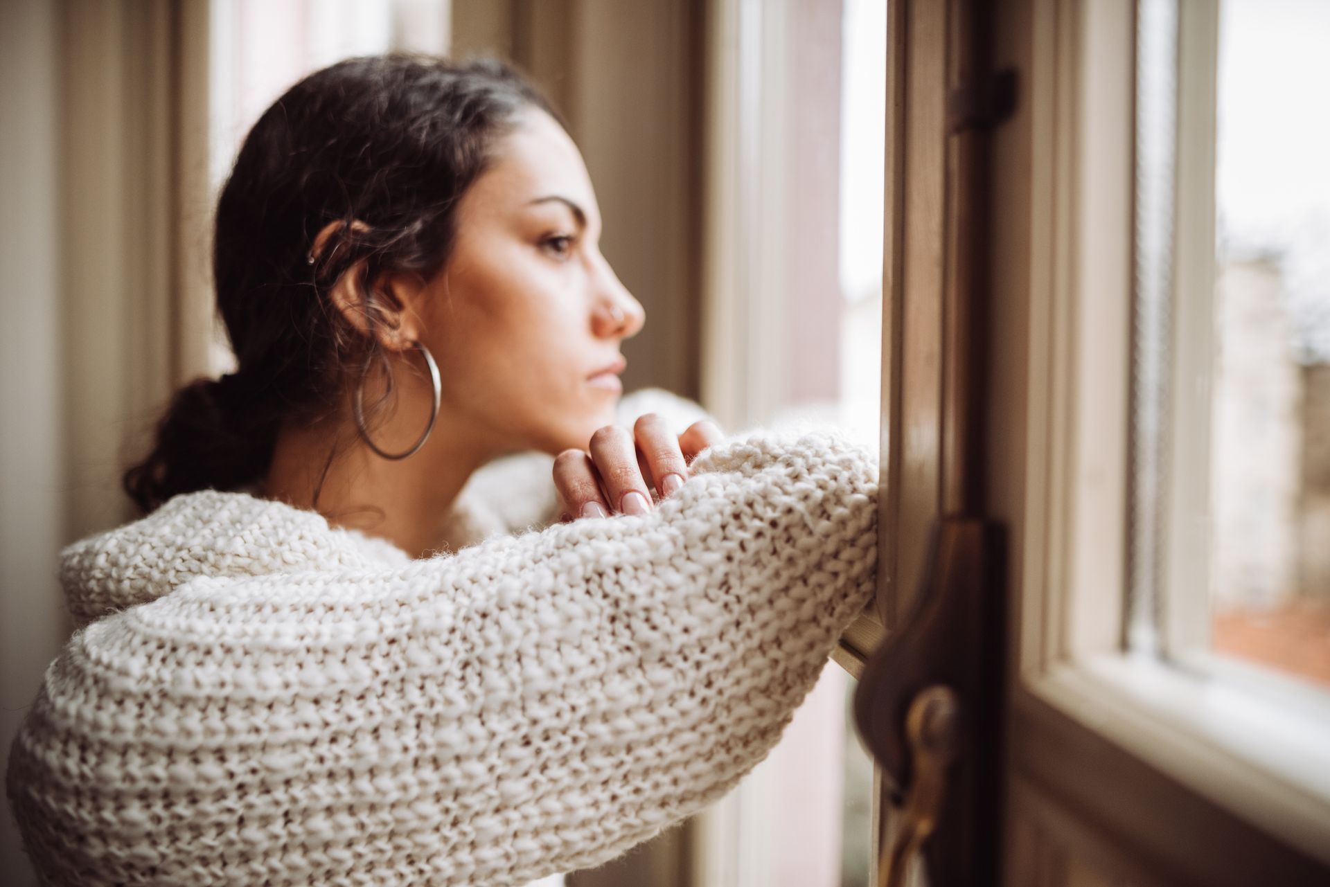 A woman in a sweater is looking out of a window.
