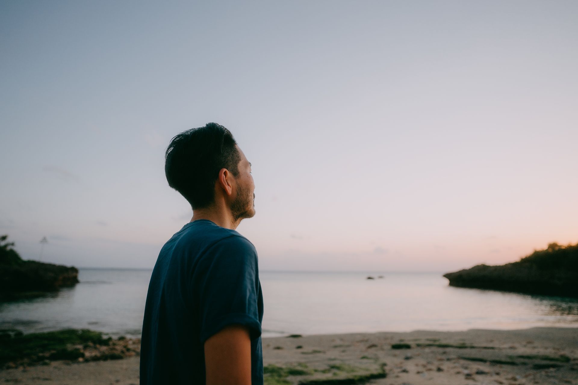 A man is standing on a beach looking at the ocean.