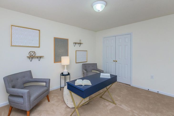 Home office: gray armchairs, blue desk, white lamp, framed art, and closet doors.