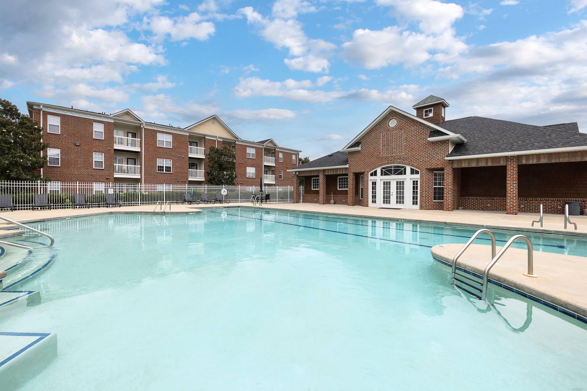 Outdoor pool with brick buildings and a blue sky.