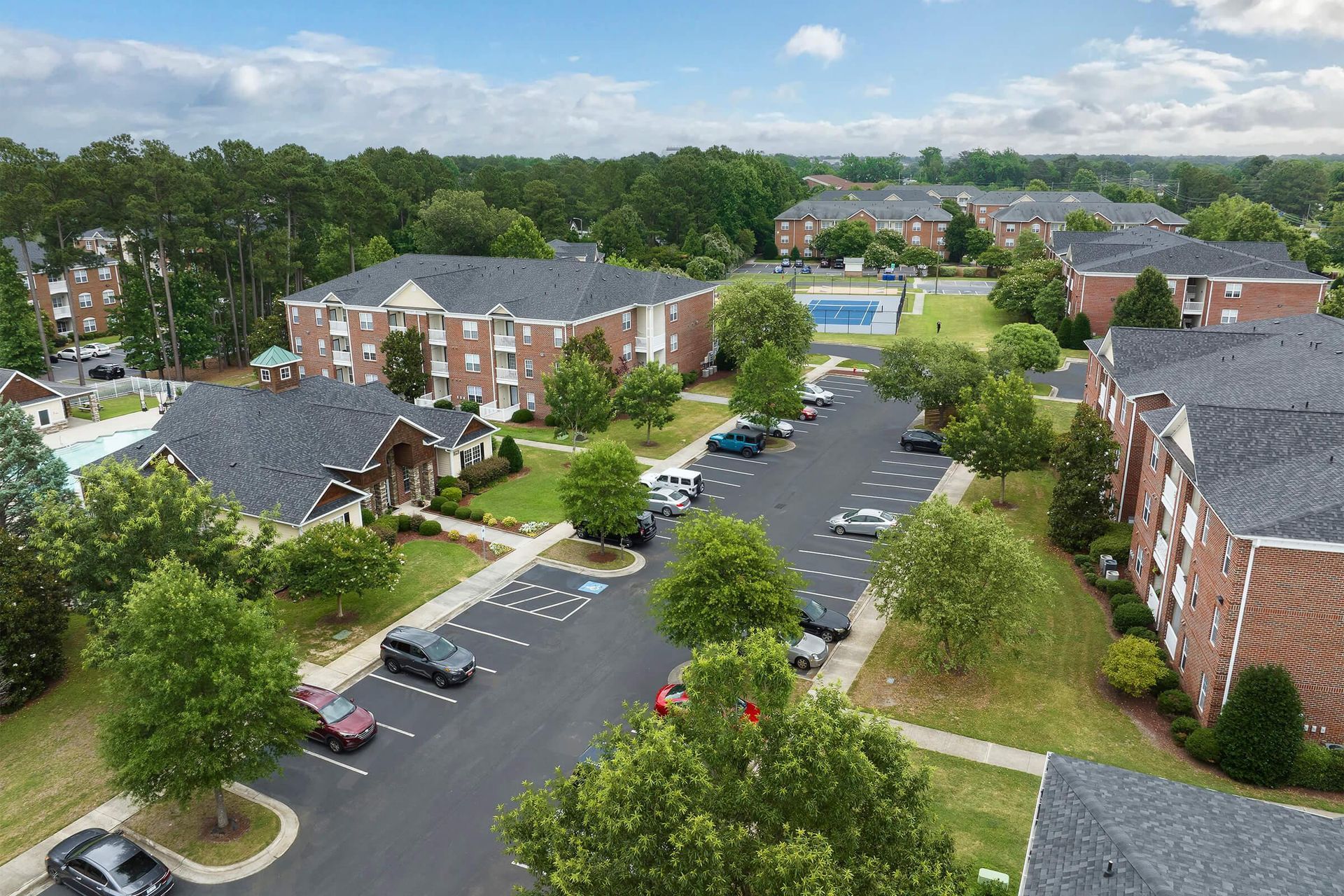 Aerial view of apartment complex with brick buildings, parking lot, and green spaces.
