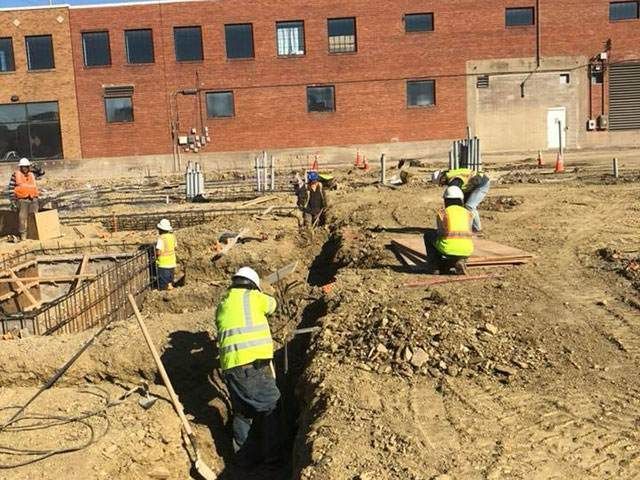 A group of construction workers are digging in the dirt in front of a brick building.