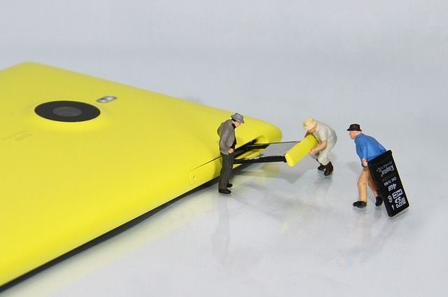 a group of miniature people are working on a yellow cell phone .