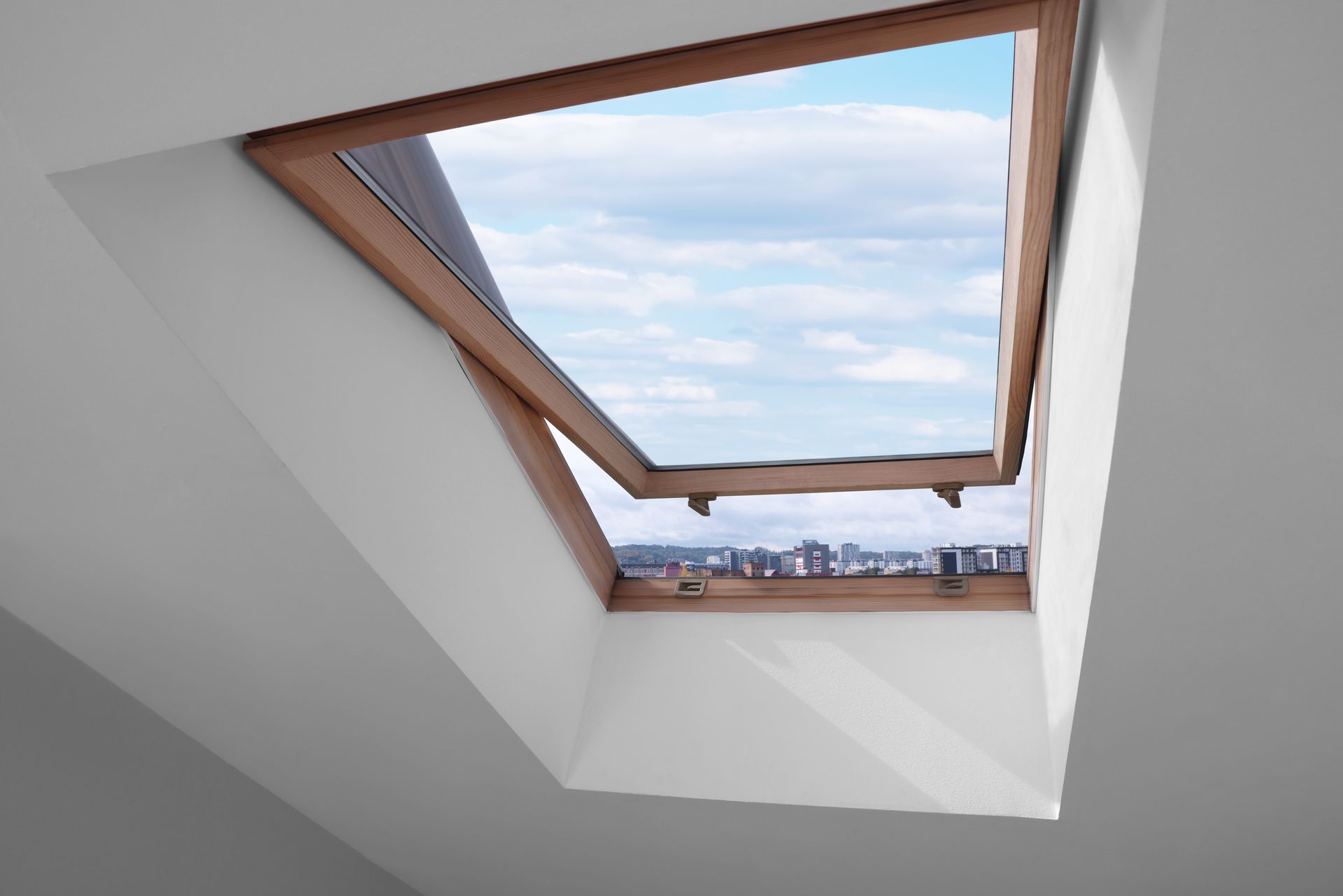Open skylight in a white-walled room, revealing a view of a city skyline and blue sky.