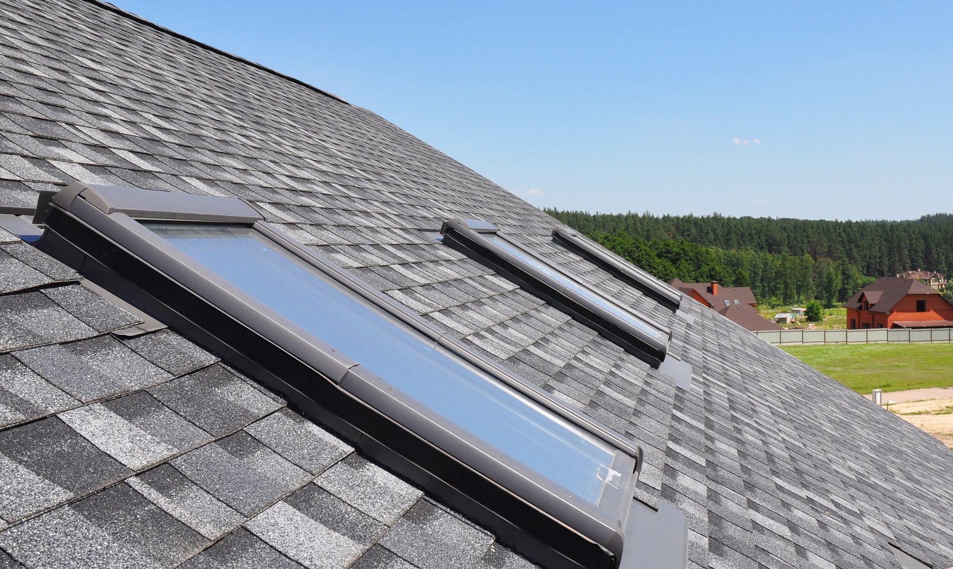 Gray shingle roof with three skylights, against a blue sky.