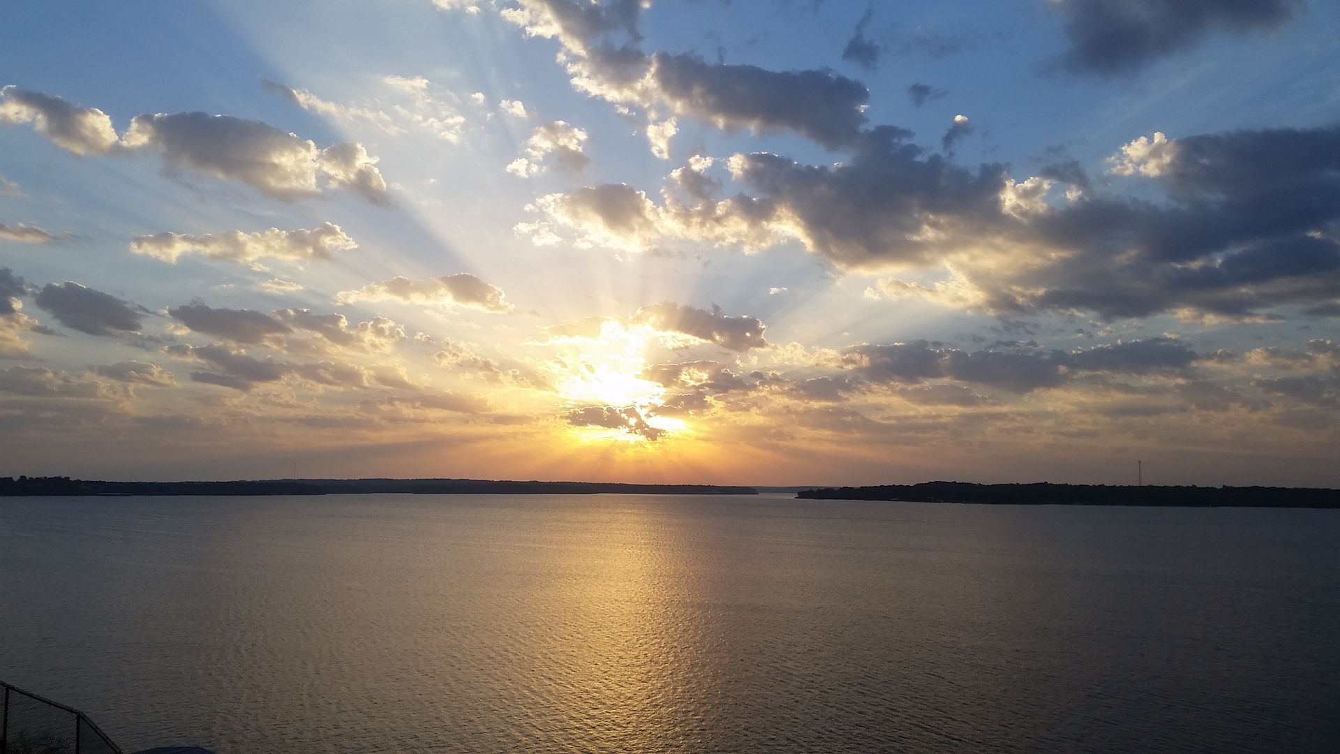 Sunset over water, with rays of sunlight breaking through clouds.