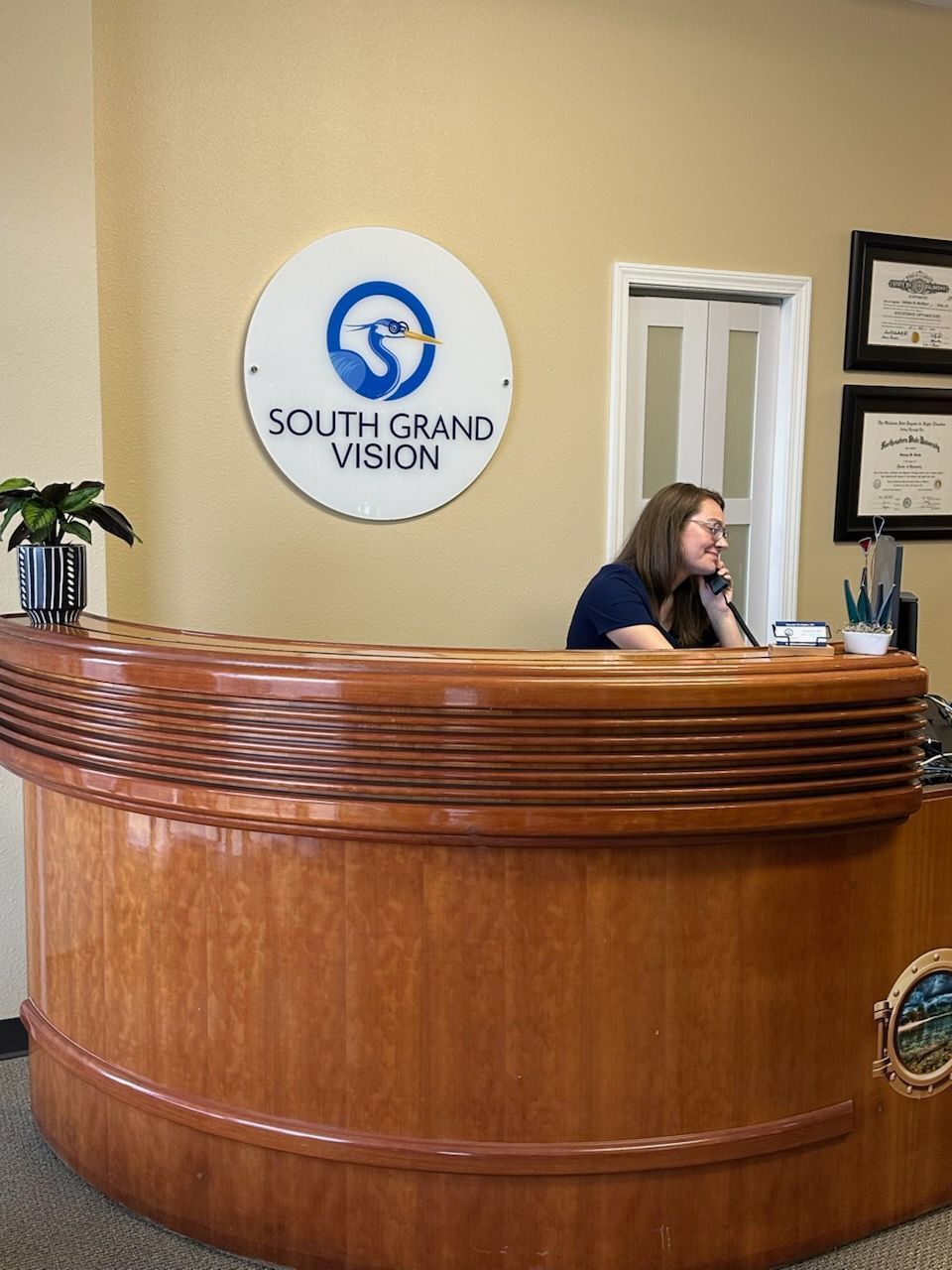 Receptionist at South Grand Vision office, answering a phone call at a wooden desk under the business sign.