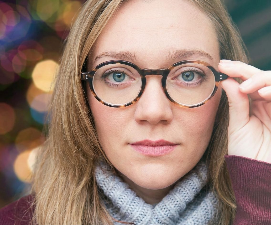 Woman with round eyeglasses, adjusting them with her finger, looking at the camera.