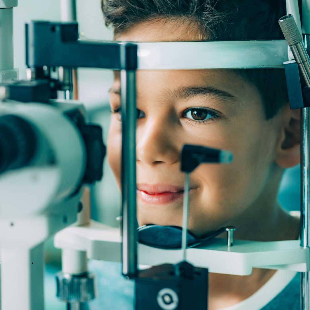 Boy undergoing an eye exam, looking through a machine.