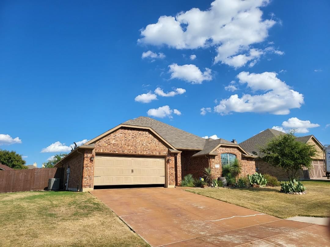 A brick house with a garage and a driveway on a sunny day.