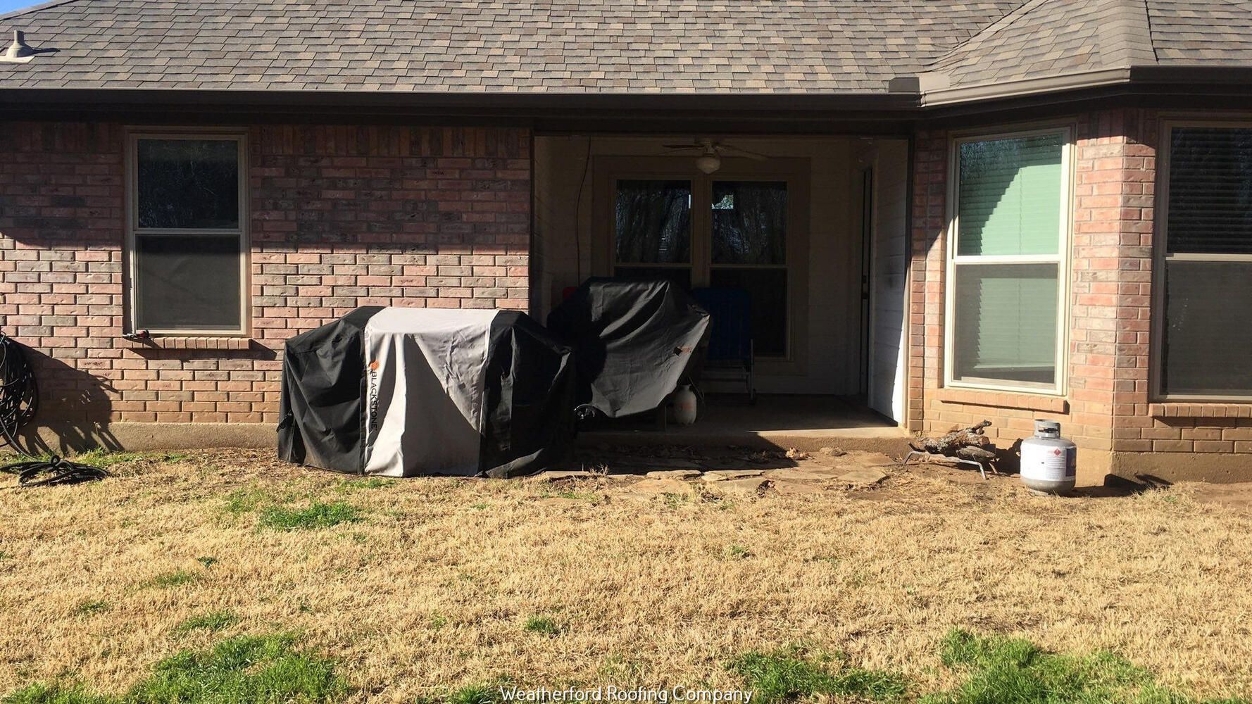 A brick house with a covered patio and a lawn in front of it.