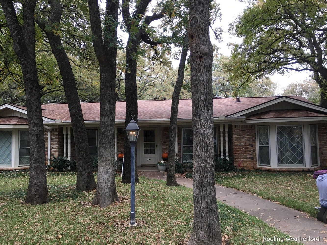 A brick house with a pink roof is surrounded by trees.