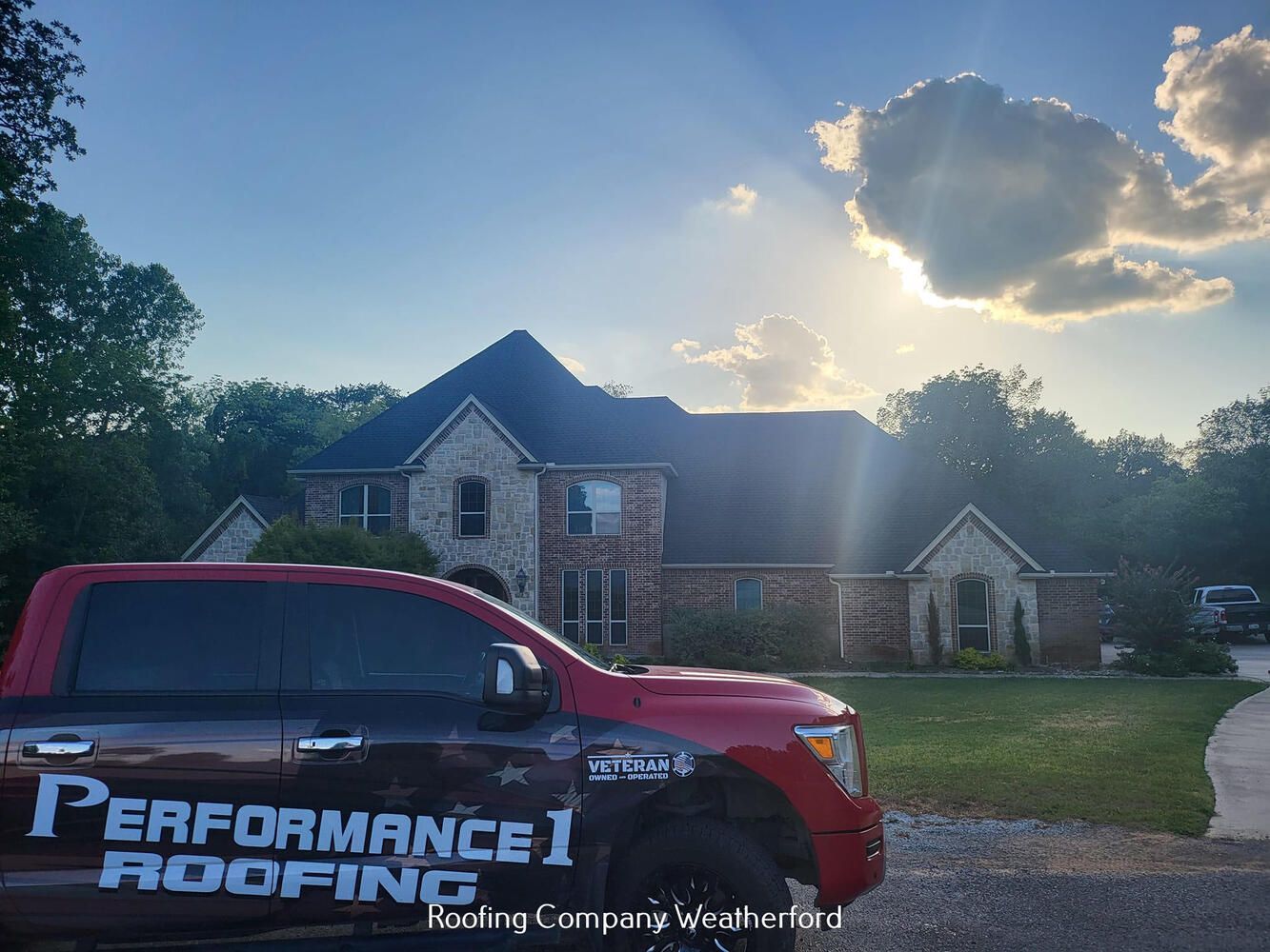 A red performance roofing truck is parked in front of a large house.