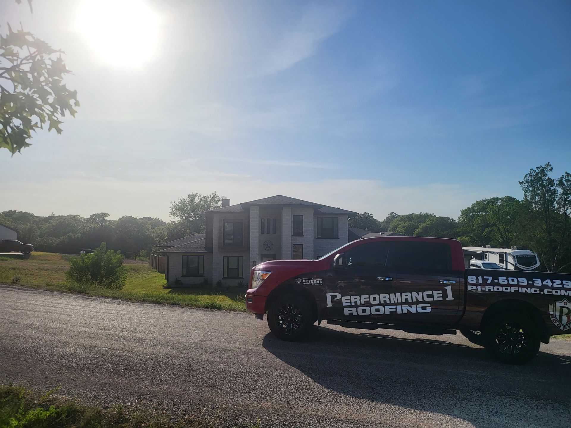 A red performance roofing truck is parked in front of a house.