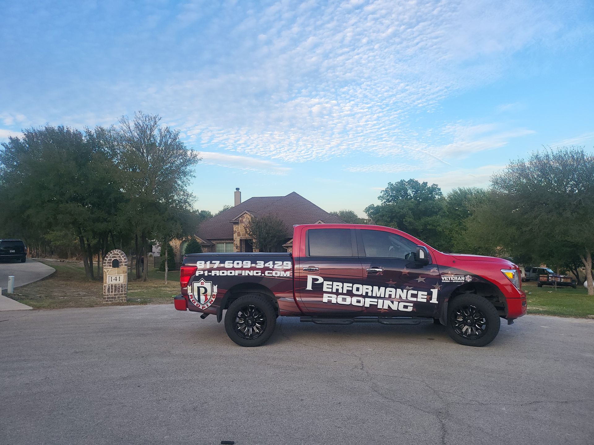 A red performance roofing truck is parked on the side of the road.