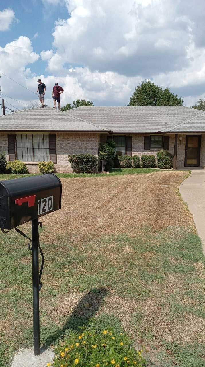 Two men are working on the roof of a house next to a mailbox.