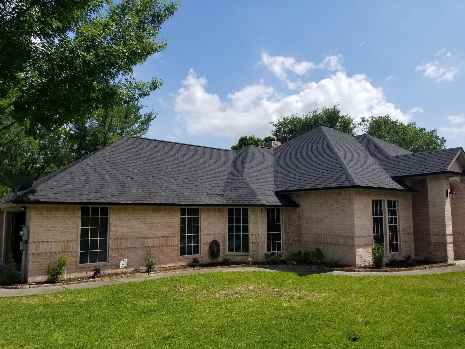 A large brick house with a black roof is sitting on top of a lush green lawn.