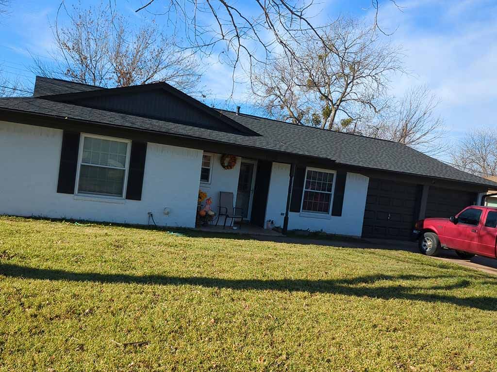 A red truck is parked in front of a white house with a black roof.