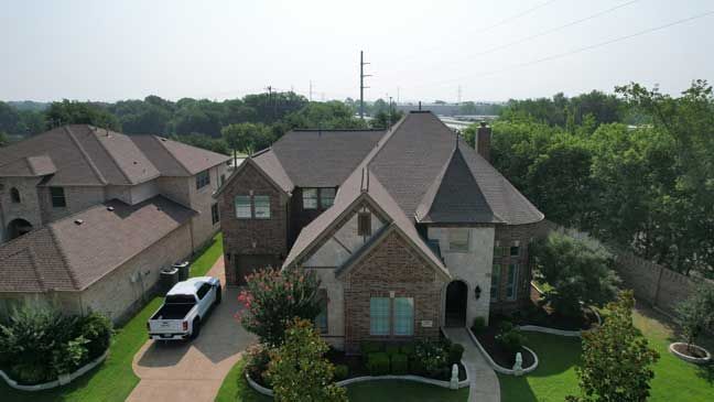 An aerial view of a large brick house with a car parked in the driveway.