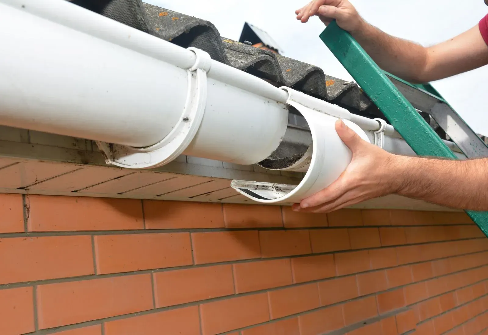 A man is installing a gutter on the side of a brick building.