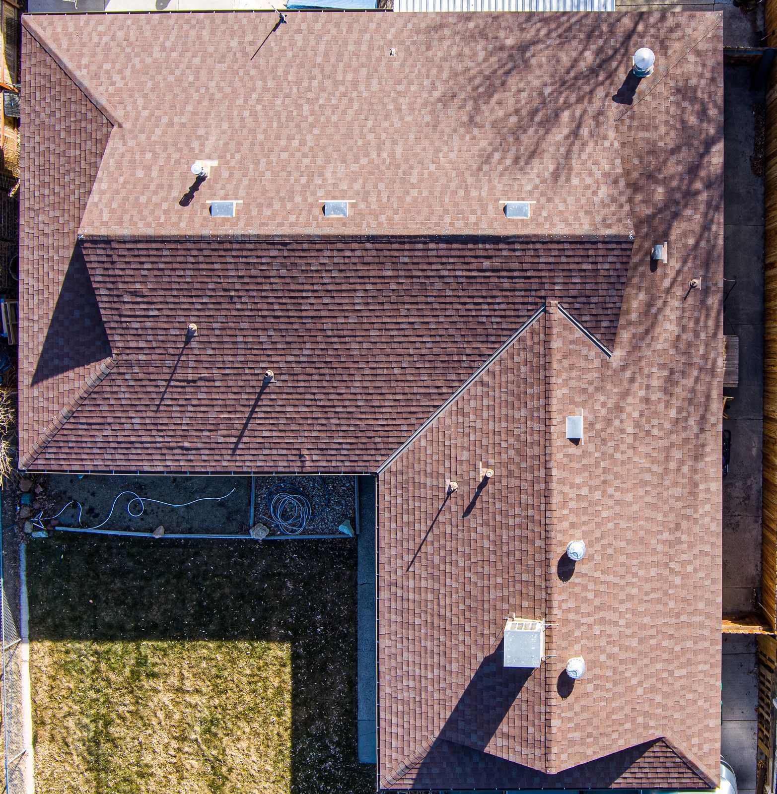 Overhead view of a brown-shingled house with multiple roof sections; yard with brown grass.