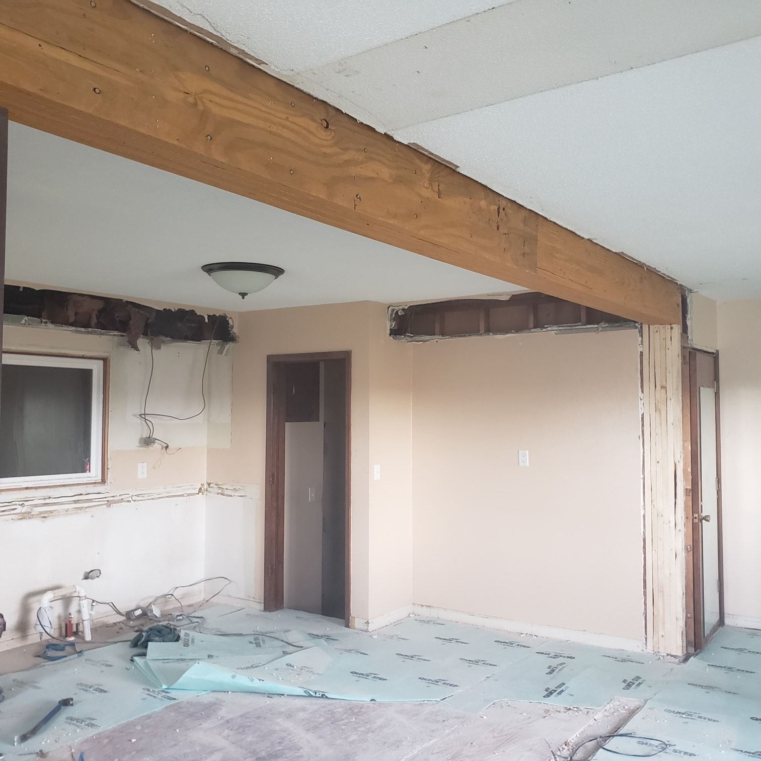 Room under renovation; exposed beams, walls, and doorway. Light blue flooring and beige walls.