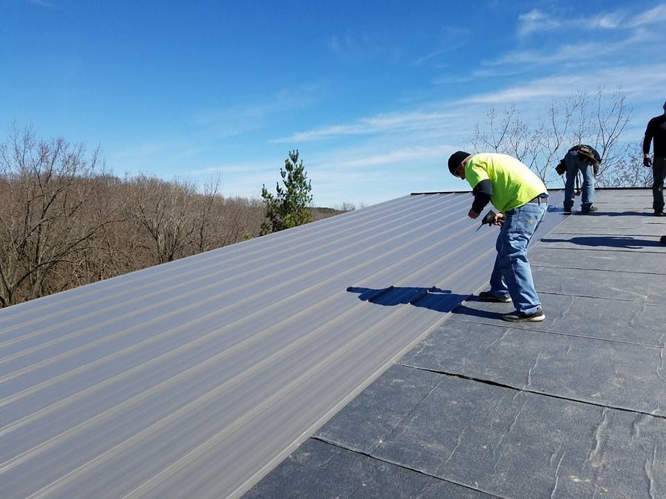 Workers installing gray metal roofing on a sunny day.