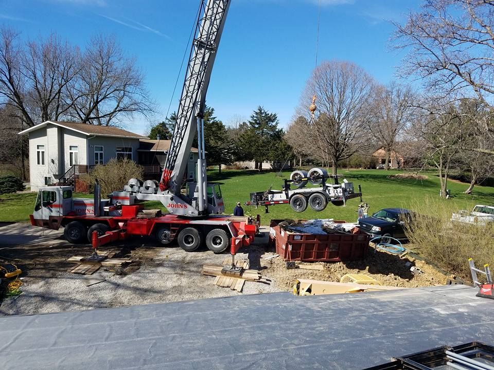 A large crane lifting equipment at a construction site near a house on a sunny day.