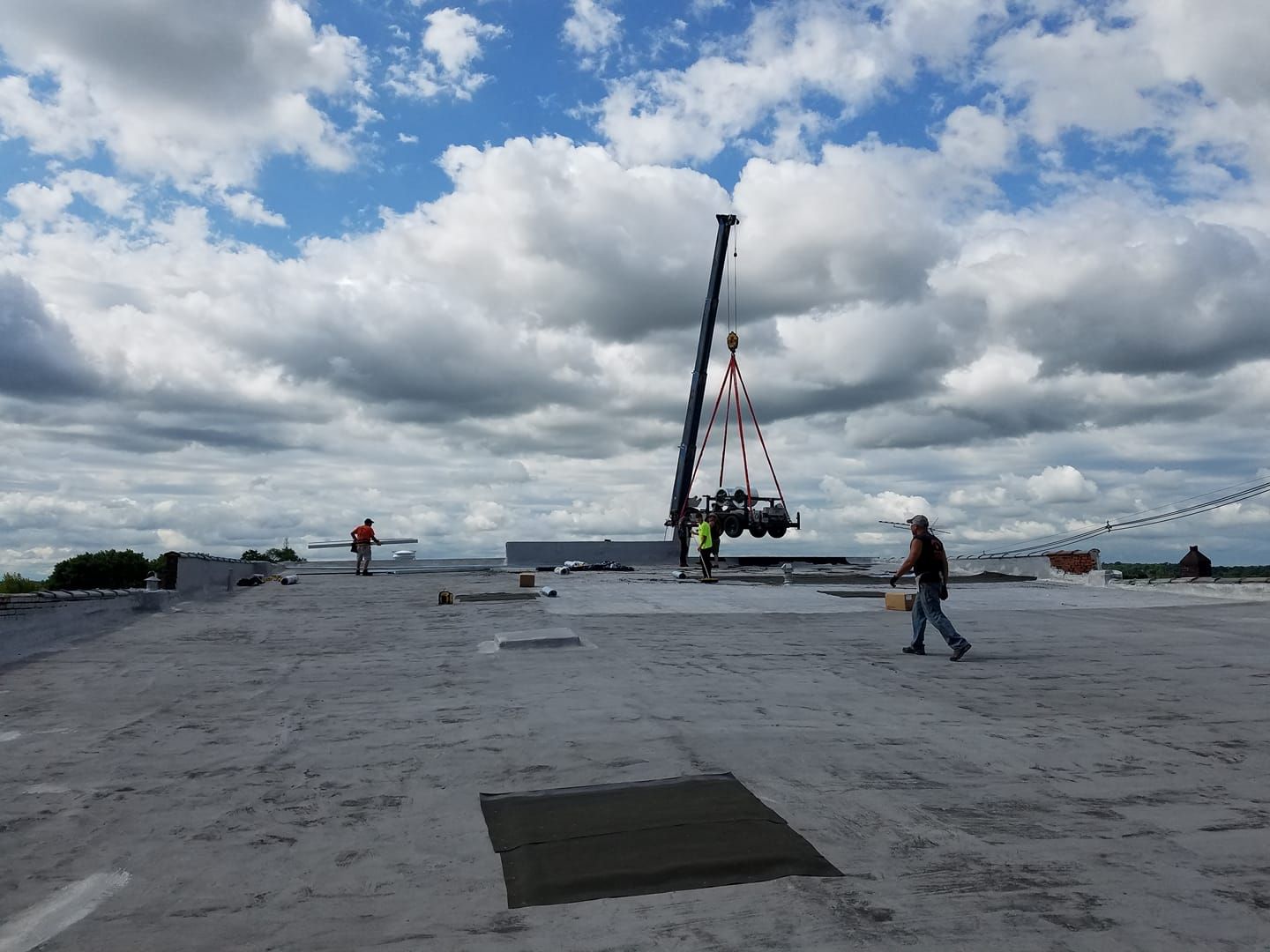 Crane lifting equipment onto a rooftop. Workers in safety gear, cloudy sky overhead.