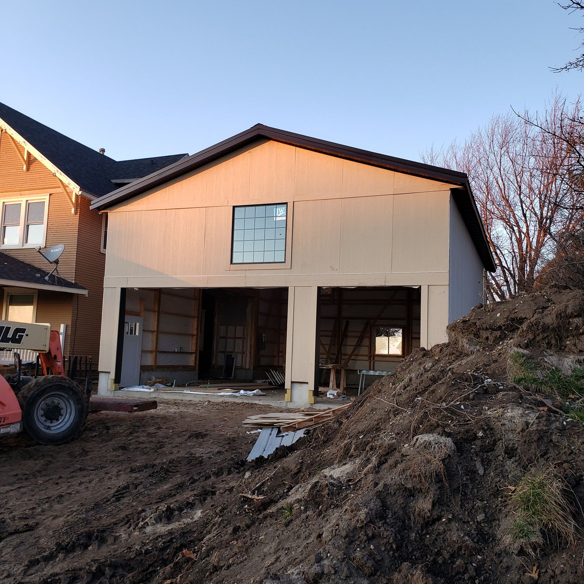 Building under construction next to a house with exposed framing and a large window.