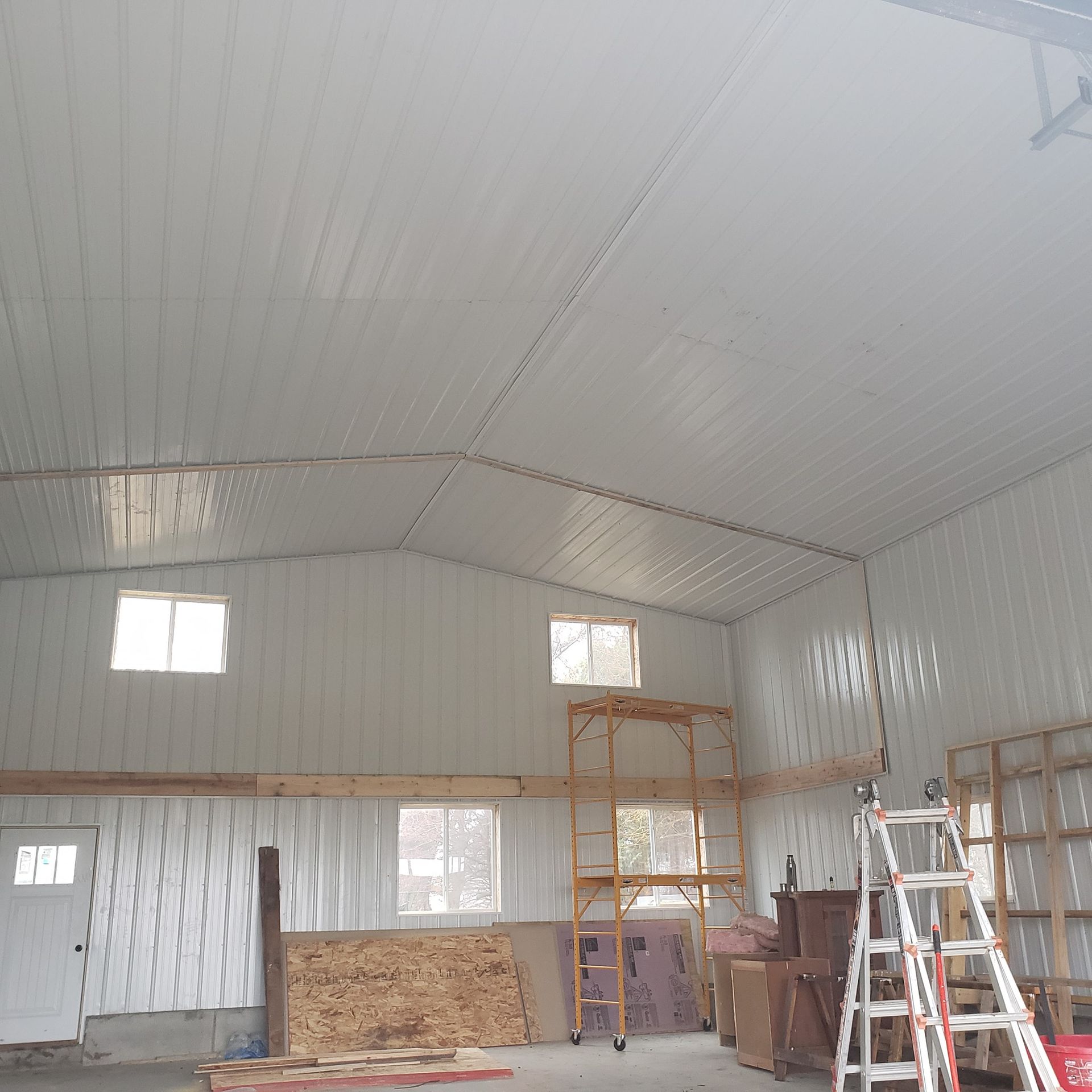 Interior of a metal building with white walls and ceiling, windows, and ladders.