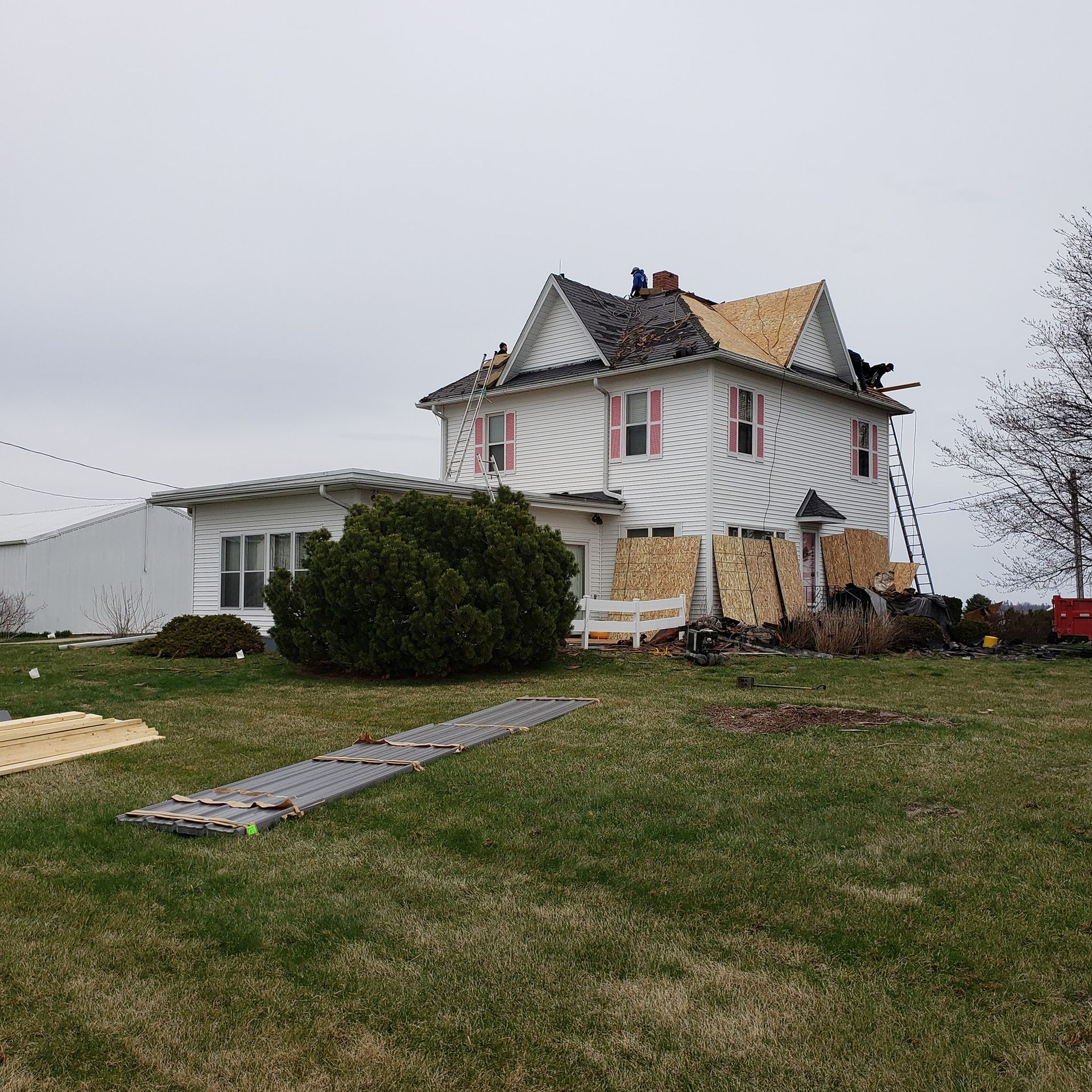 House under renovation with tarp, missing roof, and materials on the lawn.