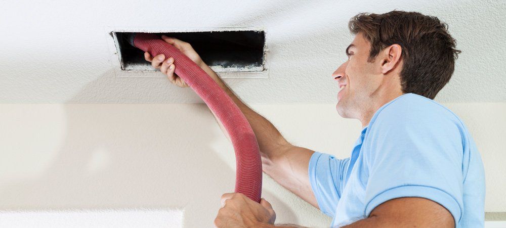 A man is cleaning an air vent with a vacuum cleaner.