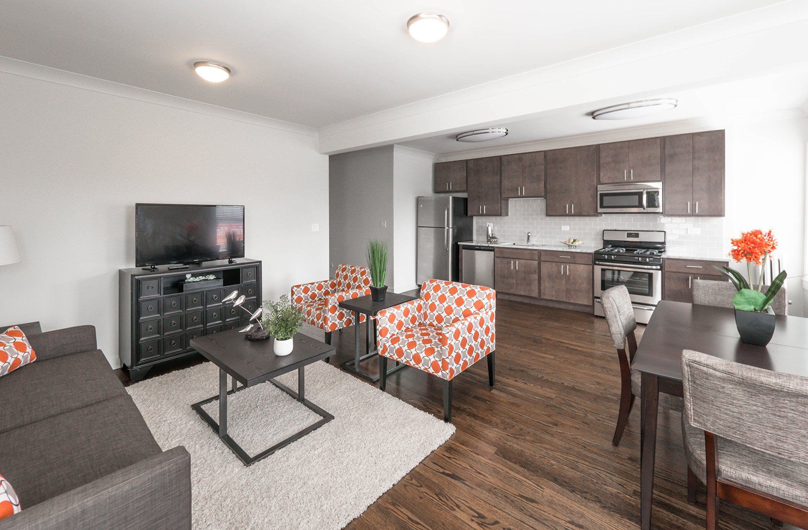 A living room and kitchen with a couch, chairs, table, cabinets, fridge, stove, and television.