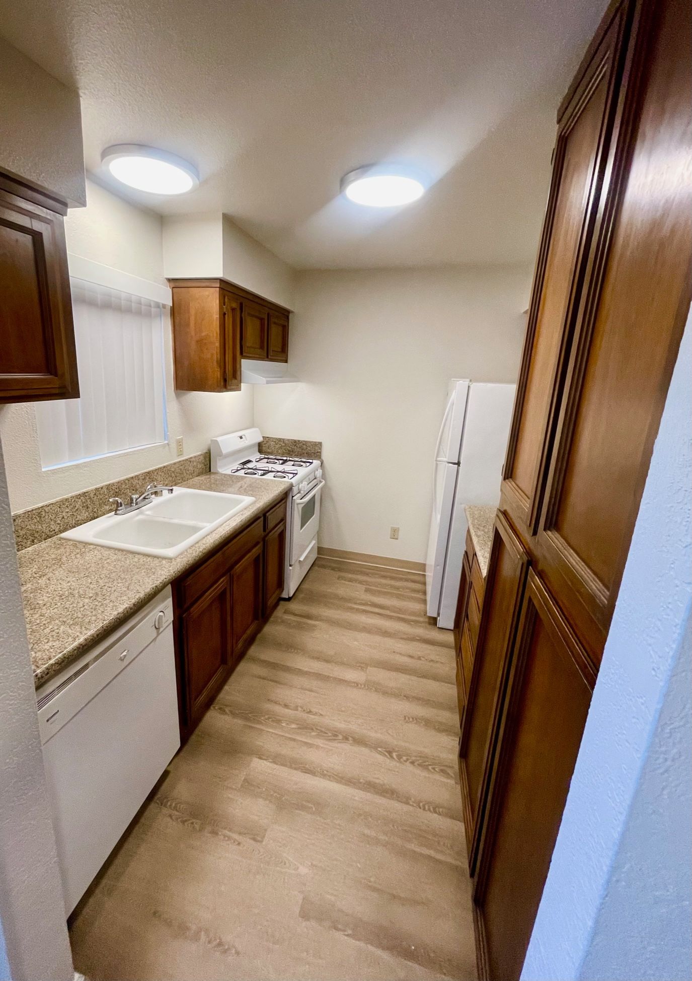 Kitchen with brown cabinets, white appliances, and beige countertops.
