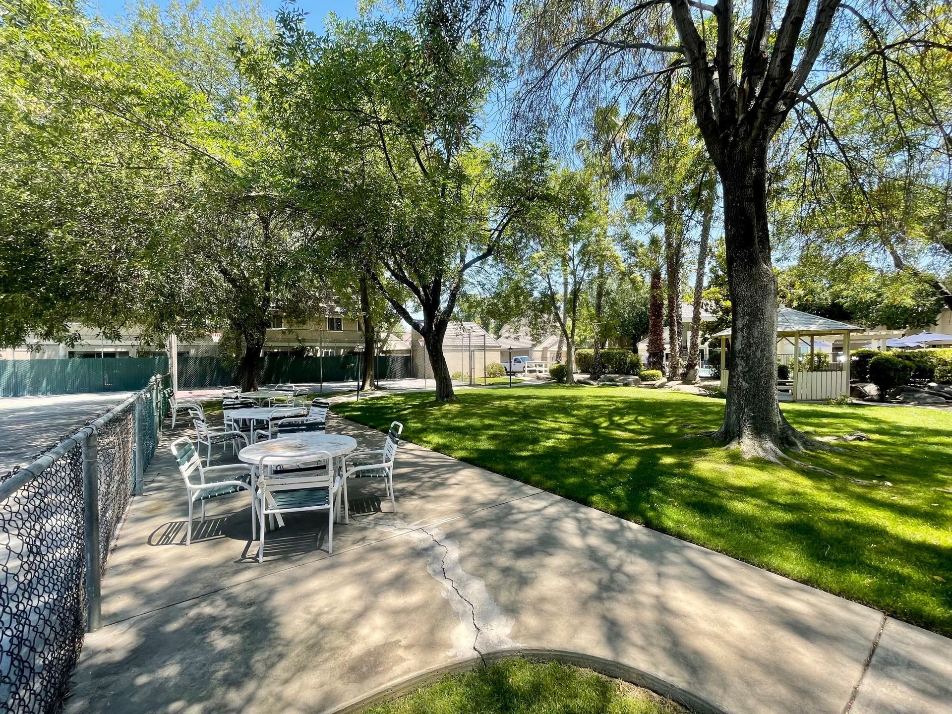 Outdoor seating area with tables, chairs, and trees in a park-like setting.