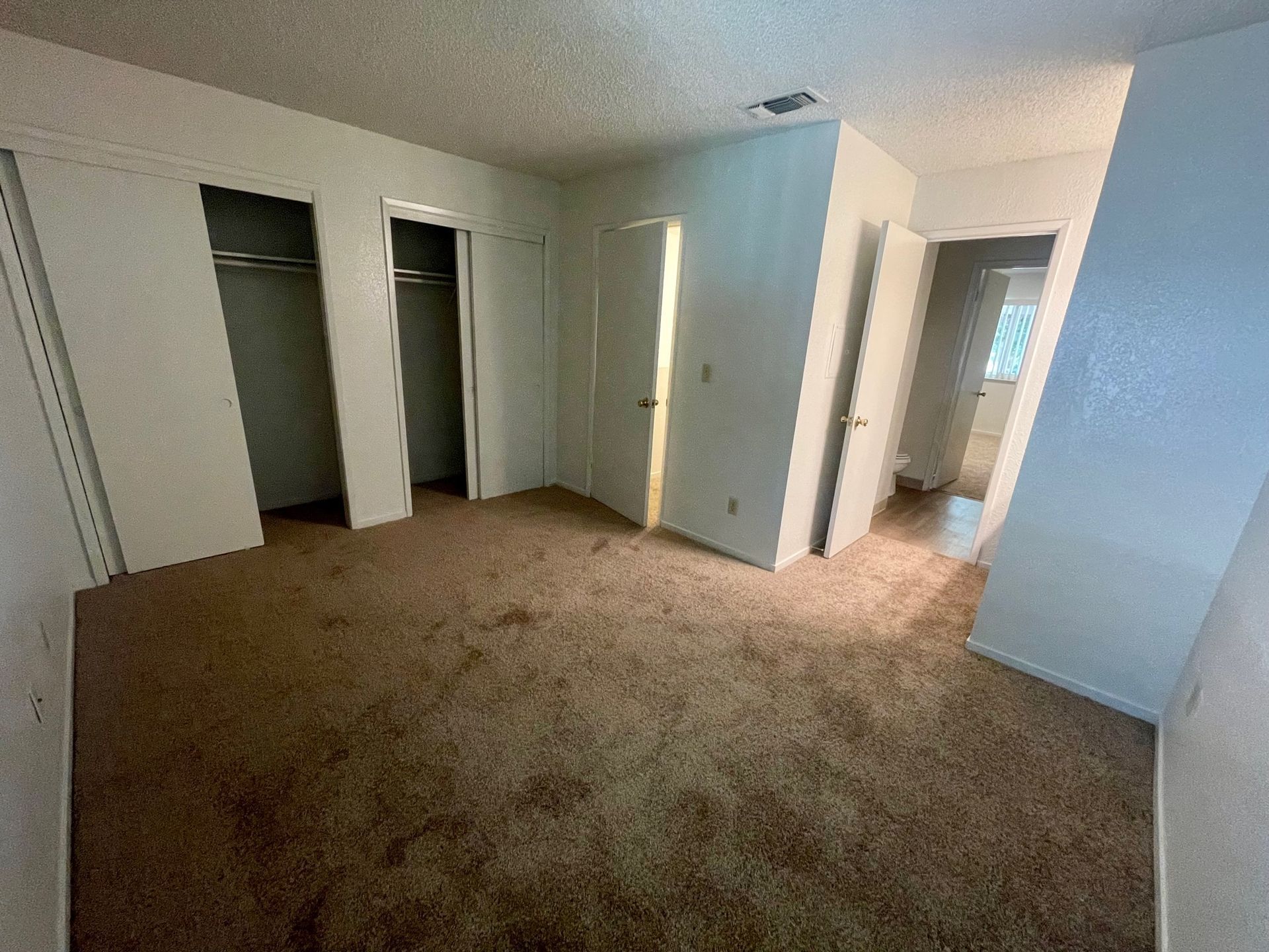Empty room with beige carpet, two closets, and a doorway.