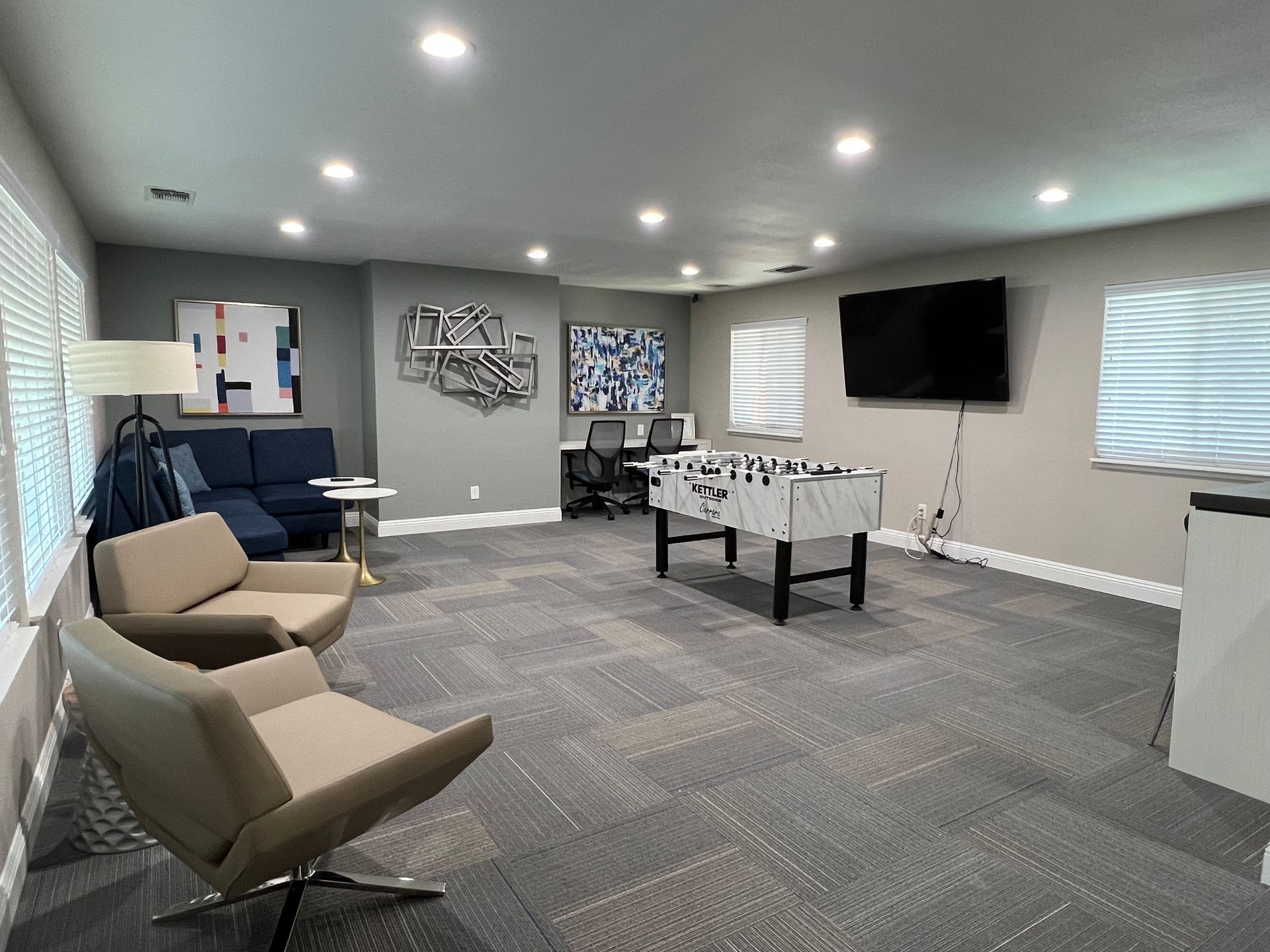 A recreational room with foosball table, TV, seating, artwork, and office space.