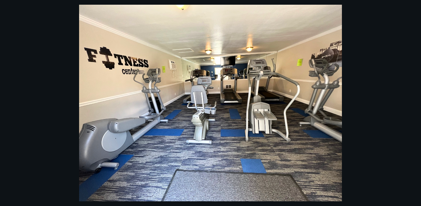 Gym with various exercise machines on patterned carpet, fitness wall decor.