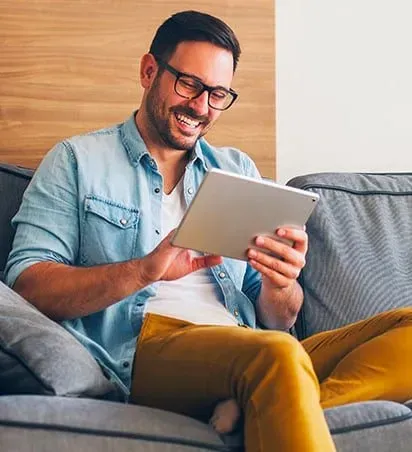 A man is sitting on a couch using a tablet computer.